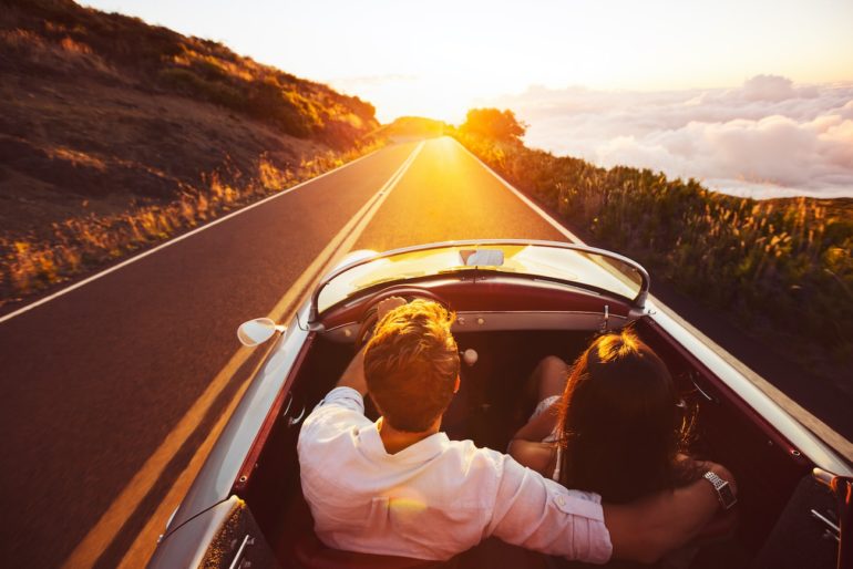 Paar fährt mit Cabrio in den Sonnenuntergang